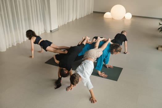 A team of children and a coach do an unusual pose at an indoor yoga workout.