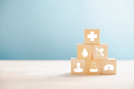 Wooden cubes crafted into a pyramid, embodying the healthcare and insurance concept. Medical insurance icon atop reflects protection. Blue background with space for promoting Health Insurance ideas.