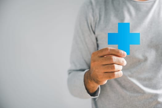 Isolated, a male hand holds a plus icon, symbolizing addition of benefits, personal growth, health insurance, and growth. It underscores innovation within health care and technology.