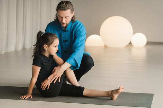 A yoga instructor in training helps a child to do exercises in the gym.