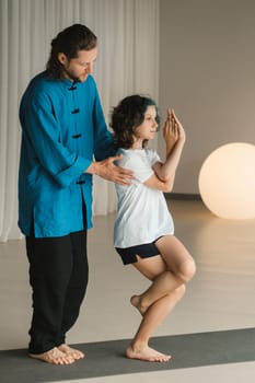 A yoga instructor in training helps a child to do exercises in the gym.