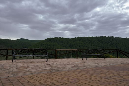 Two lonely benches in a fresh mountain landscape. No people, iron, forge, sun with clouds, pine forest, relaxation, go wood,