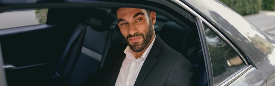 Male entrepreneur sitting on car backseat and working with documents while going to office