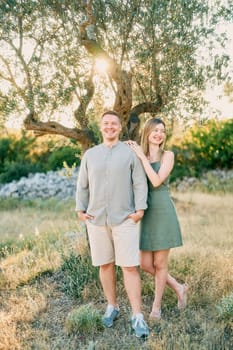 Young woman stands with her hands on the shoulder of laughing man and looks away. High quality photo