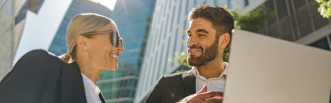 Business colleagues working on project while sitting outdoors on skyscrapers background