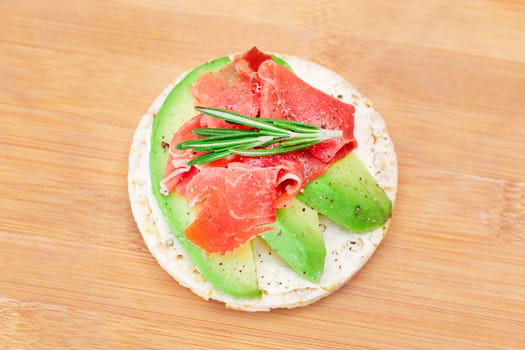 Rice Cake Sandwich with Fresh Avocado, Jamon and Rosemary on Bamboo Cutting Board. Easy Breakfast. Diet Food. Quick and Healthy Sandwiches. Crispbread with Tasty Filling. Healthy Dietary Snack