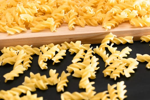Uncooked Fusilli Pasta Scattered on Wooden Board and Black Table. Raw and Dry Macaroni. Fat and Unhealthy Food
