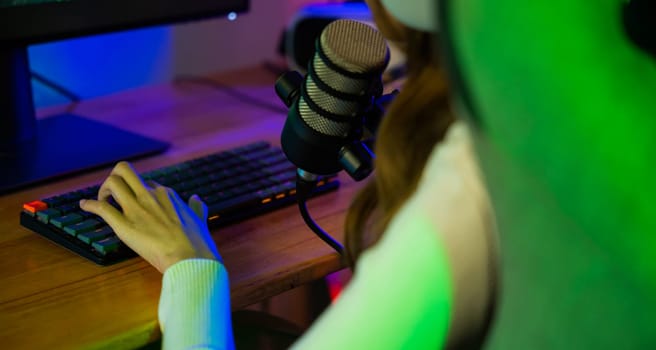 Asian young gamer woman press on keyboard to playing video games online on computer she live stream and chat with fans, Streamer female talking with microphone in gaming room, game streaming concept
