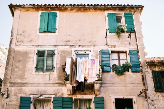 Colorful laundry dries on lines on the balcony of an ancient stone house with green wooden shutters. High quality photo