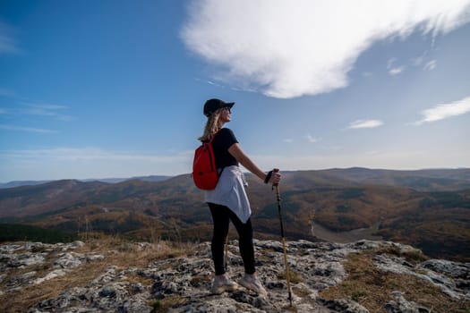 woman on mountain peak looking in beautiful mountain valley in autumn. Landscape with sporty young woman, blu sky in fall. Hiking. Nature.