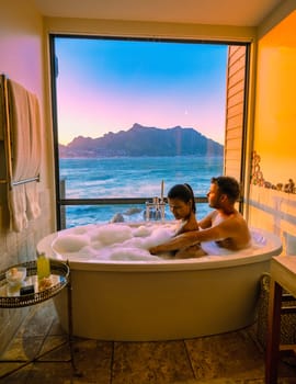 a couple of men and women in the bathtub looking out over the ocean of Cape Town South Africa during vacation. Bath Tub during sunset, man and woman in bathtub on vacation