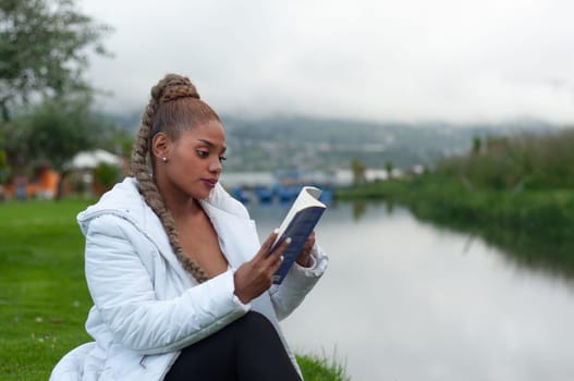 copyspace of a latin woman in a white jacket sitting by a river relaxing reading a book. book day. High quality photo