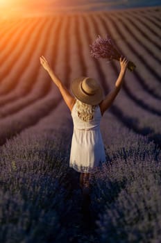 Blonde woman poses in lavender field at sunset. Happy woman in white dress holds lavender bouquet. Aromatherapy concept, lavender oil, photo session in lavender.