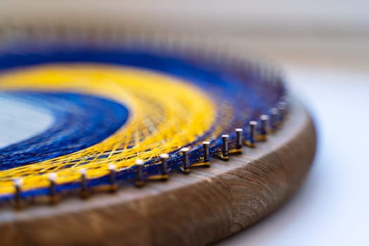 Colored thread mandala on a wooden board with nails. Mandala Moon Harmony Sun esotericism and psychology pictures from yellow and blue silk threads