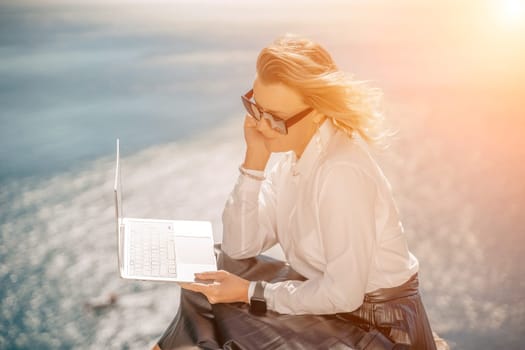 Business woman on nature in white shirt and black skirt. She works with an iPad in the open air with a beautiful view of the sea. The concept of remote work