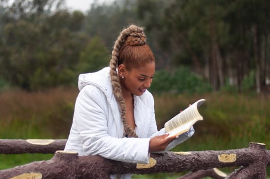 latin woman from ecuador leaning on the trunks of a wooden bridge while reading a very interesting book while smiling. book day. High quality photo