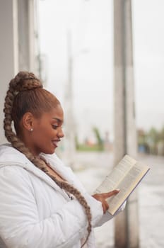 vertical photo of beautiful latina woman leaning against a wall happily reading a book with a big smile on her face. book day. High quality photo
