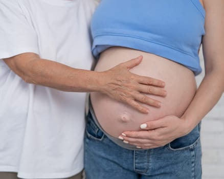 An elderly woman touches the belly of her pregnant daughter. Close-up