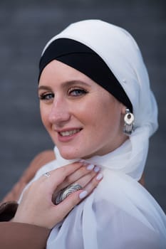 Portrait of a young blue-eyed woman in a hijab against a gray brick wall