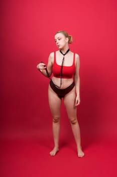Seductive blonde female with leash standing in a studio, red background
