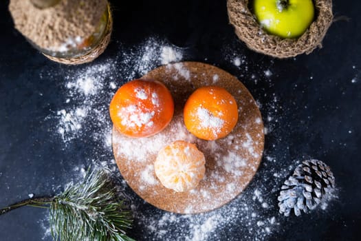 Green apples tangerines and pine cones on a table, dark background