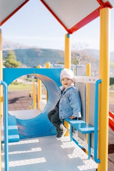 Little smiling girl sitting on a bench on a slide. High quality photo