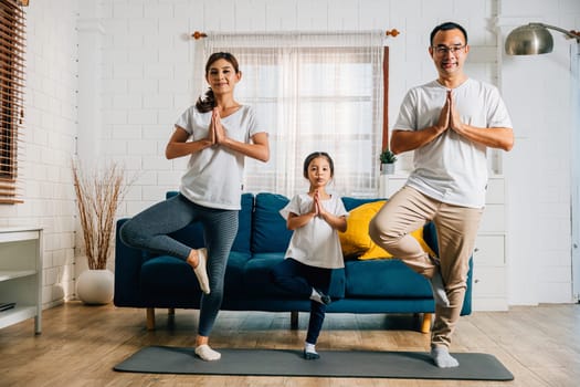 A family weekend at home becomes a harmonious and joyful experience as Asian parents and their daughter practice yoga and fitness promoting health happiness and togetherness.