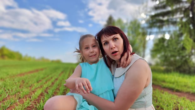 Happy mother and daughter enjoying rest, playing and fun on nature in green field. Woman and girl resting outdoors in summer or spring day