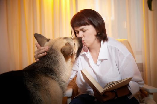 Adult mature woman with big shepherd dog in white shirt. Room with girl and calm cozy evening atmosphere with transparent curtains and soft warm light of lamps. Concept of love for animals, pets