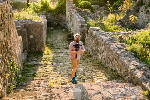 Cameraman in summer outfit with gimbal and cinema camera in his hands making travel video with old europe Balkan nature on the background.