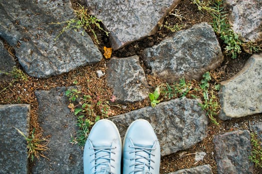 Women's legs in blue shoes on the stone pavement, top view. Photo pov. Copy space and empty place for text.