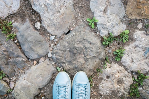 Women's legs in blue shoes on the stone pavement, top view. Photo pov. Copy space and empty place for text.