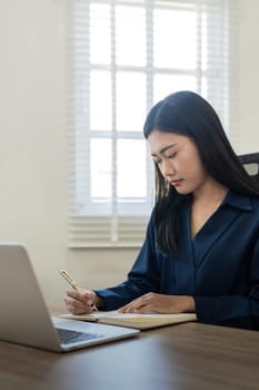 Entrepreneur working online with a laptop and taking notes in a notebook in home.