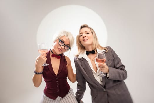 two close girlfriends with glasses of alcohol having fun laughing at a party in the studio on a white background copy paste