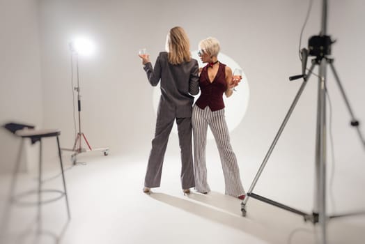 two close girlfriends with glasses of alcohol having fun laughing at a party in the studio on a white background copy paste