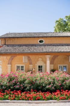 Blooming flowerbed near an ancient yellow villa with a brown tiled roof. High quality photo