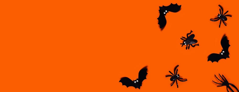 Halloween web banner - orange background with spiders, bats, hand. Flat lay with a place for your text. Plastic toys.