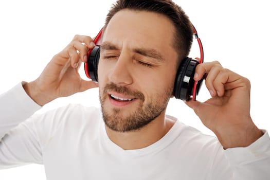 Close-up portrait of handsome young man in headphones listening to music and dancing isolated on white background.