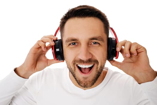 Close-up portrait of handsome young man in headphones listening to music and dancing isolated on white background.