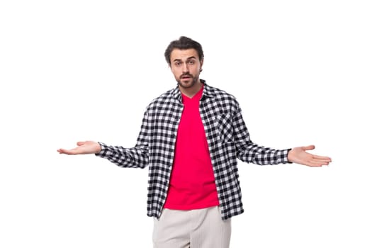 a handsome young european man with black hair and an unshaven beard in a shirt throws up his hands.