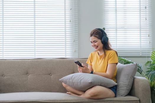 Happy asian woman listening to music from mobile phone while sitting on the the sofa at homes, Smiling girl relaxing with headphones in morning, Time to relax..