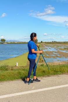 Latina woman, Active individual with walking poles next to a water body on a sunny day, Hispanic Latina woman walking with trekking poles in the Ebro Delta natural park, Tarragona, Catalonia, Spain,