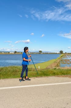 Mature adult Hispanic woman walking with trekking poles in the Ebro Delta natural park,Tarragona, Catalonia, Spain