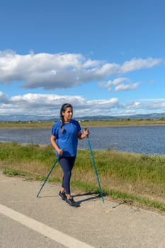 Outdoor enthusiast with walking poles beside a tranquil water body on a bright day, Hispanic Latina woman walking with trekking poles in the Ebro Delta natural park, Tarragona, Catalonia, Spain,