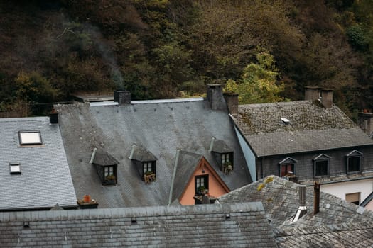 Residential antique house stands close to grey roof tiled buildings in Luxemburg. Smoke comes from chimney because of house heating during cold days