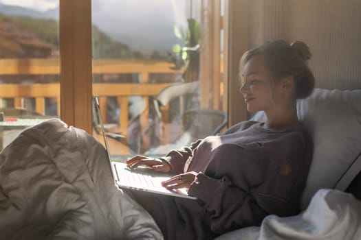 Happy casual beautiful woman working on a laptop sitting on the bed in the house