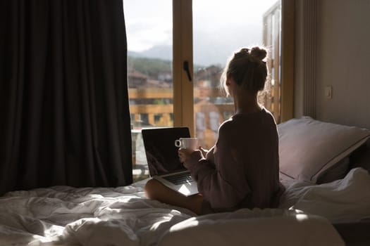 Happy casual beautiful woman working on a laptop sitting on the bed in the house