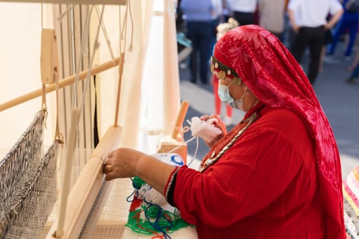 UFA, RUSSIA - JULY 10, 2021: Bashkir woman make carpet during Folkloriada in Ufa