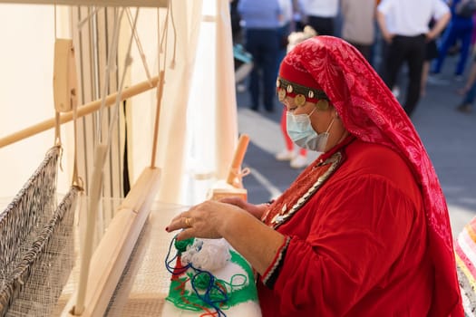 UFA, RUSSIA - JULY 10, 2021: Bashkir woman make carpet during Folkloriada in Ufa