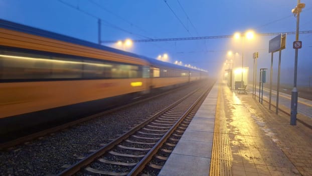 A passenger train entering the station in the fog. Night train passing the station. The concept of rail passenger transport. Night passenger train in fog.